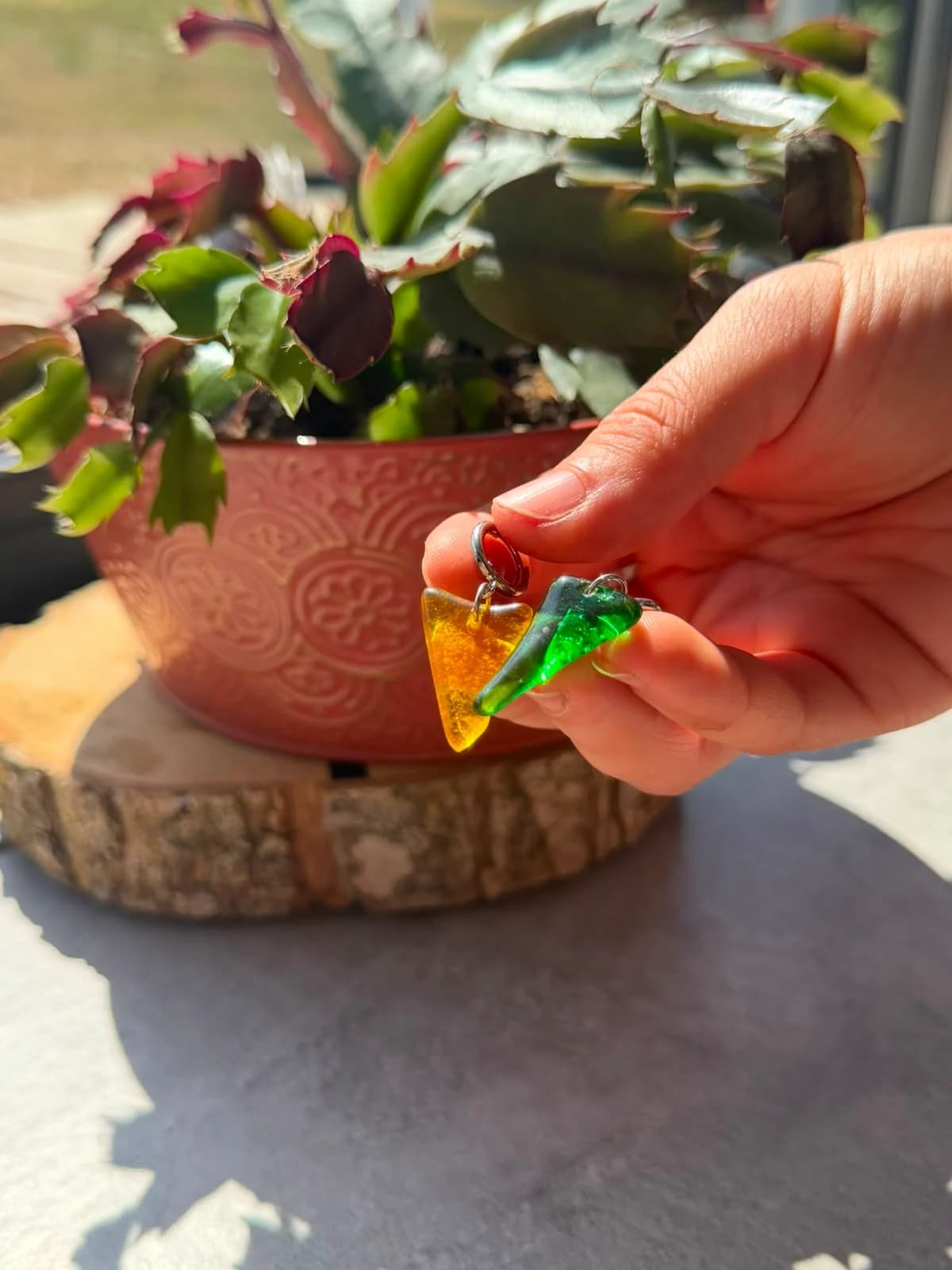 Boucles d'oreilles dormeuses en verre vert et jaune posées sur une rondelle de bois.