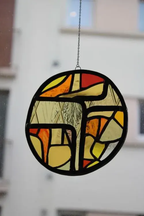 Vitrail rond artisanal aux verres ambrés et texturés suspendu devant une fenêtre lumineuse.