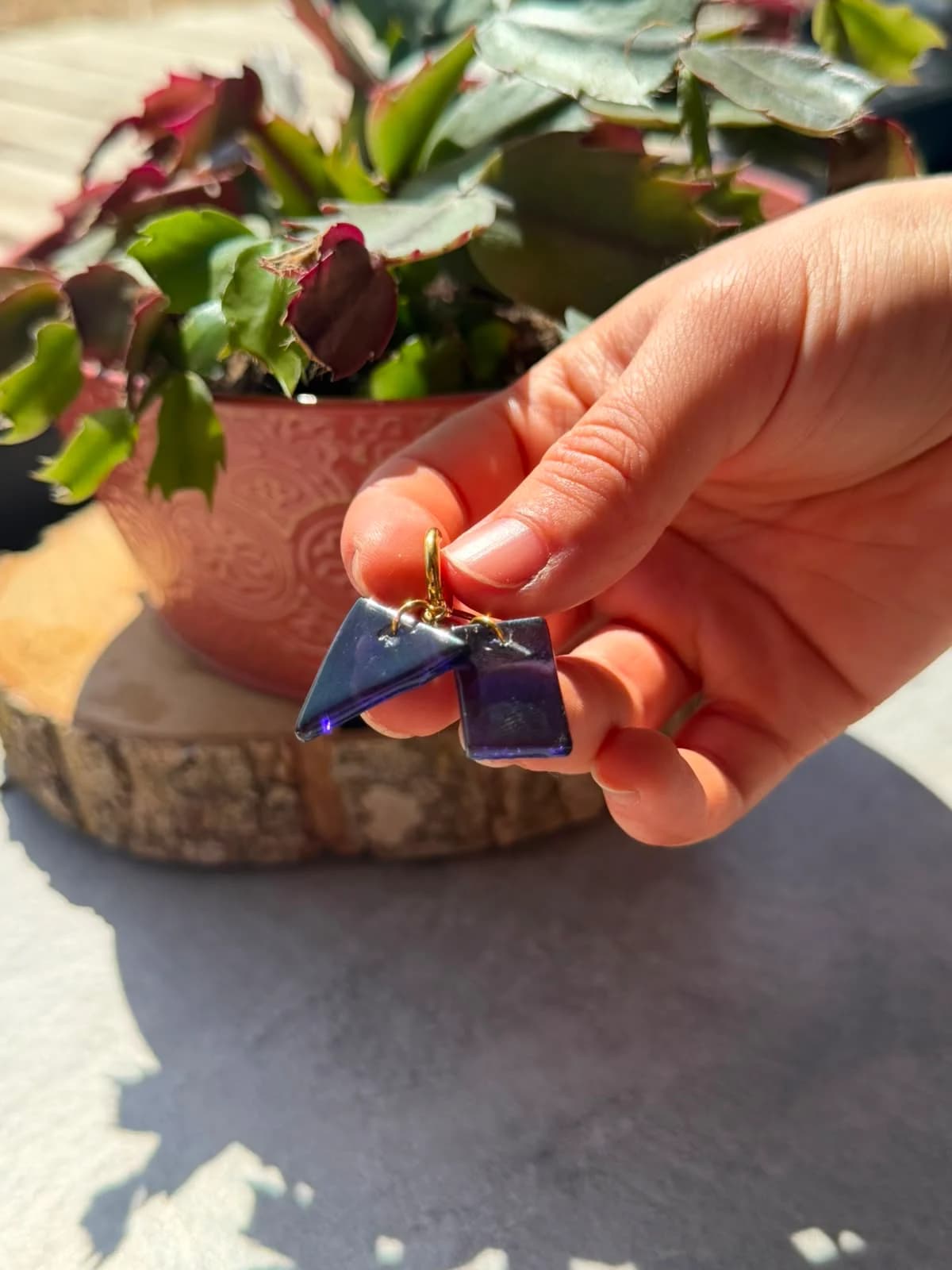 Boucles d'oreilles asymétriques en verre violet, triangle et rectangle, posées sur un disque de bois.