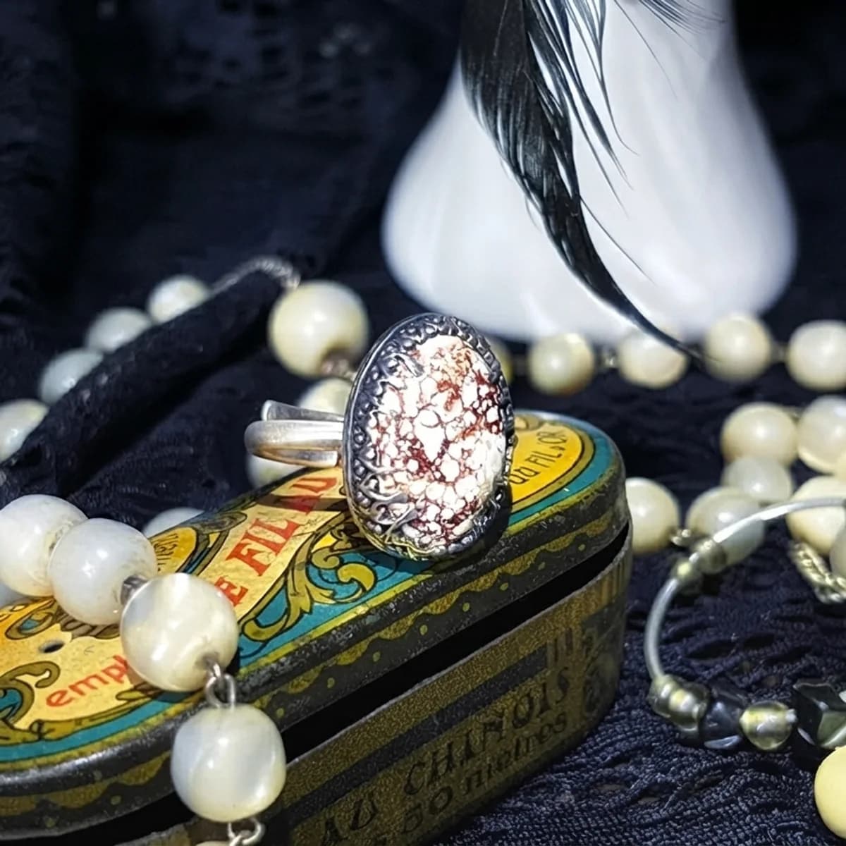 Gros plan sur une bague ovale avec pierre mouchetée sertie d'argent, posée sur une petite boîte vintage