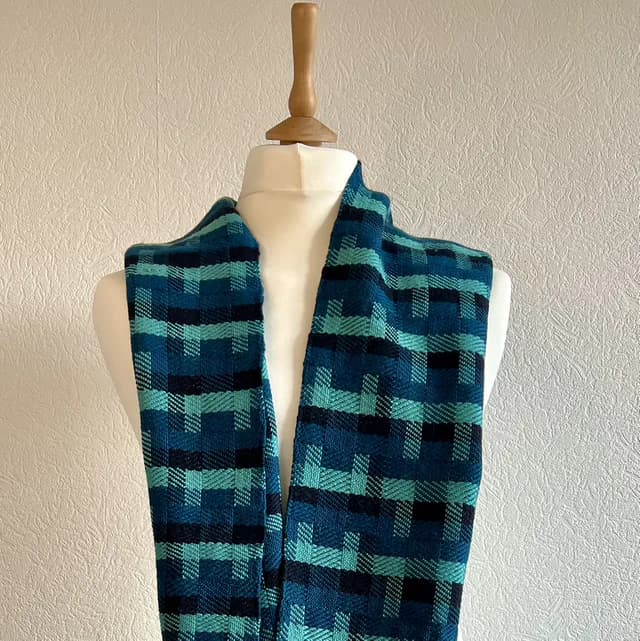 Écharpe tissée main bleue, bleu canard et noire présentée sur un buste mannequin blanc.