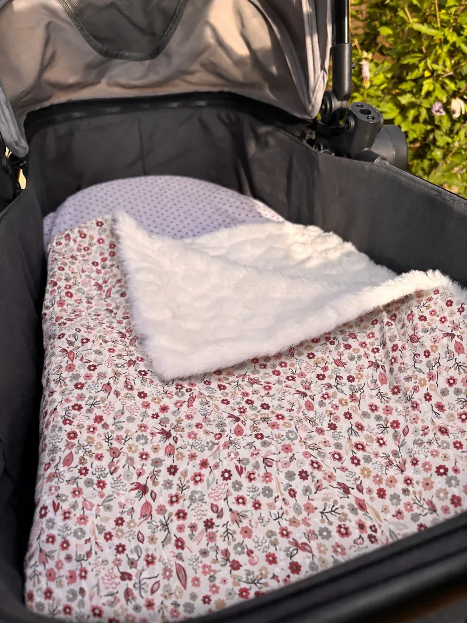 Couverture bébé à motif fleuri rose et revers polaire blanc, installée dans un landau de poussette.