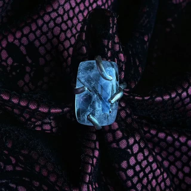 Bague en argent avec pierre de quartz et inclusions noires sur tissu à motifs.