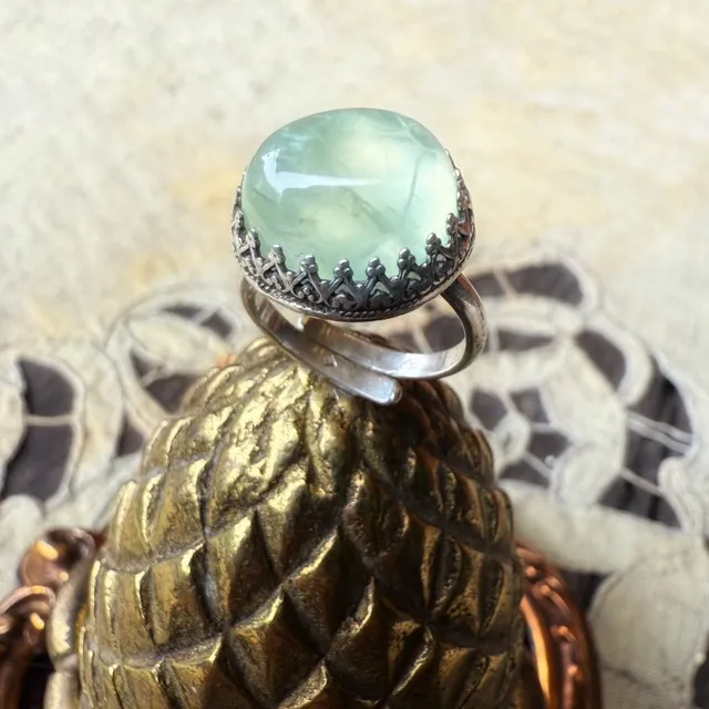 Bague en argent avec pierre cabochon vert d'eau et serti dentelé, posée sur un support doré