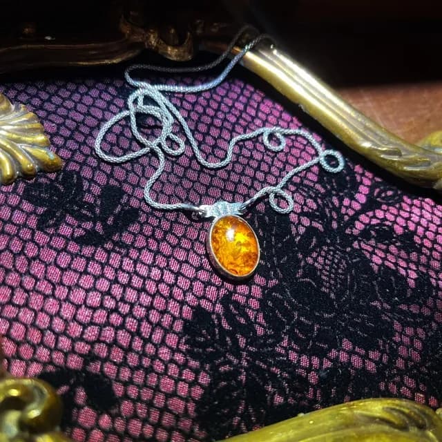Collier avec cabochon d'ambre jaune et chaîne argentée posé sur un tissu en dentelle noire et violette