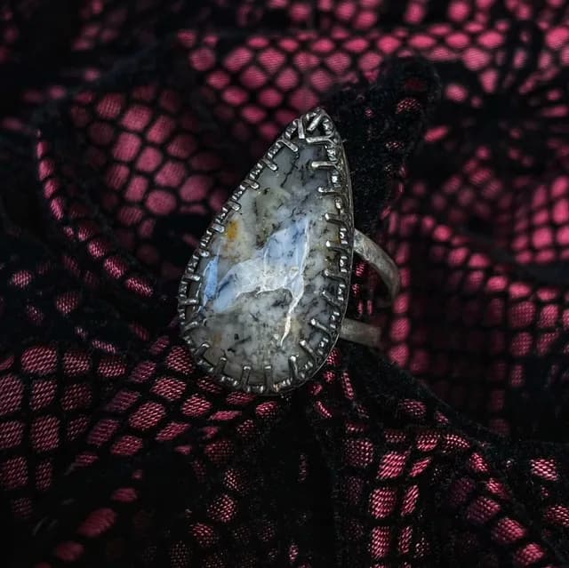 Bague en argent ornée d'une agate dendrite en goutte, posée sur une dentelle noire et rouge.