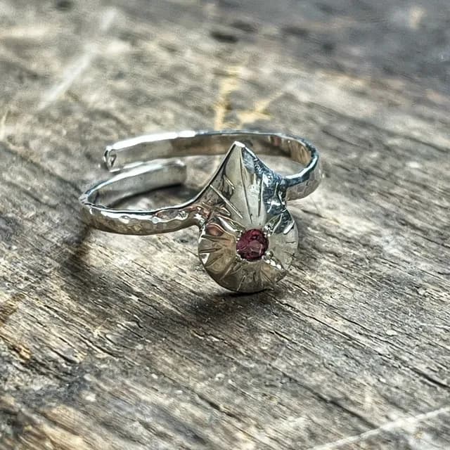 Bague réglable en argent ornée d'une pierre rose centrale taillée, posée sur du bois brut.