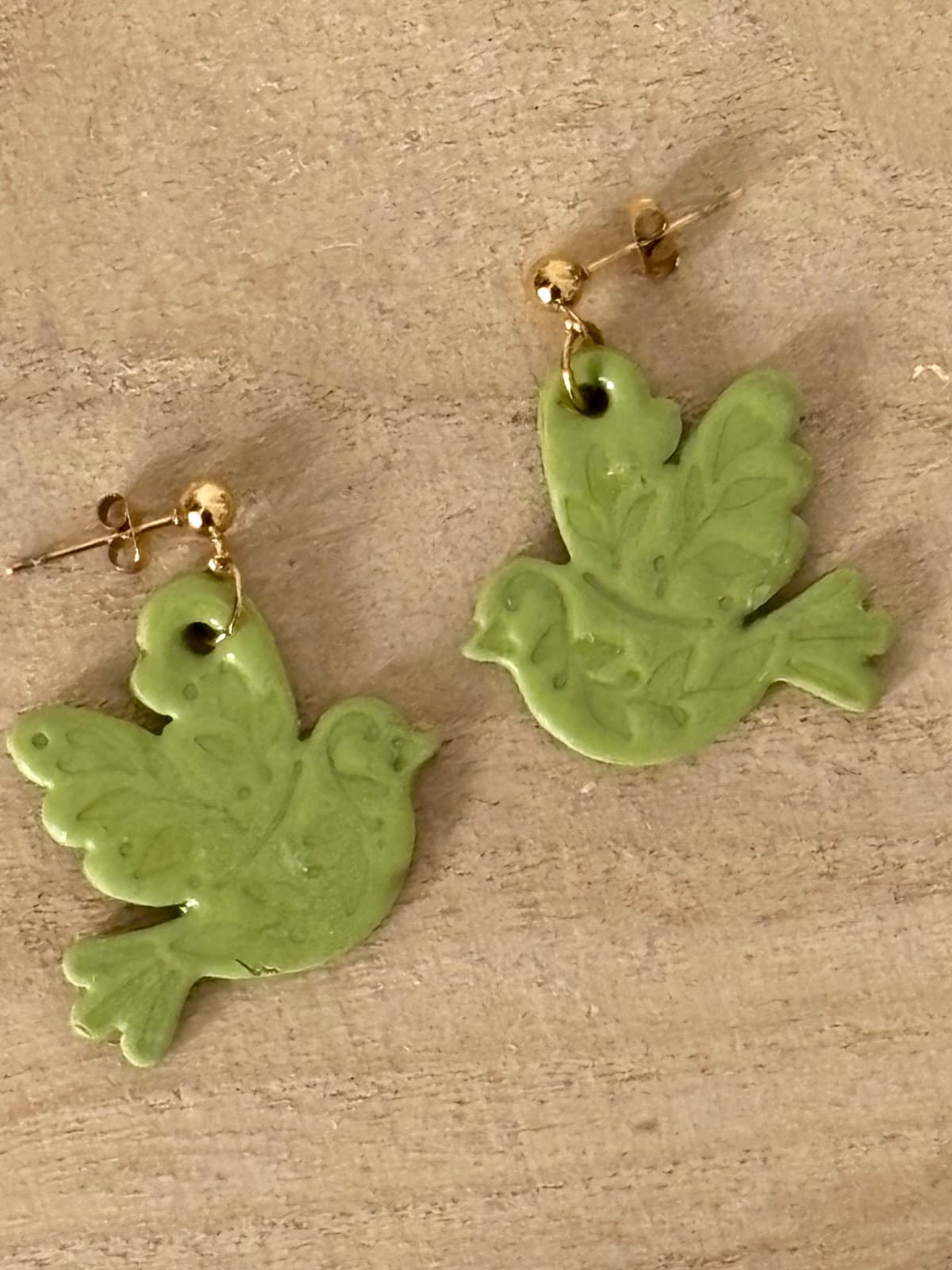 Paire de boucles d’oreilles en forme d’oiseaux vert olive avec motifs végétaux sur fond en bois
