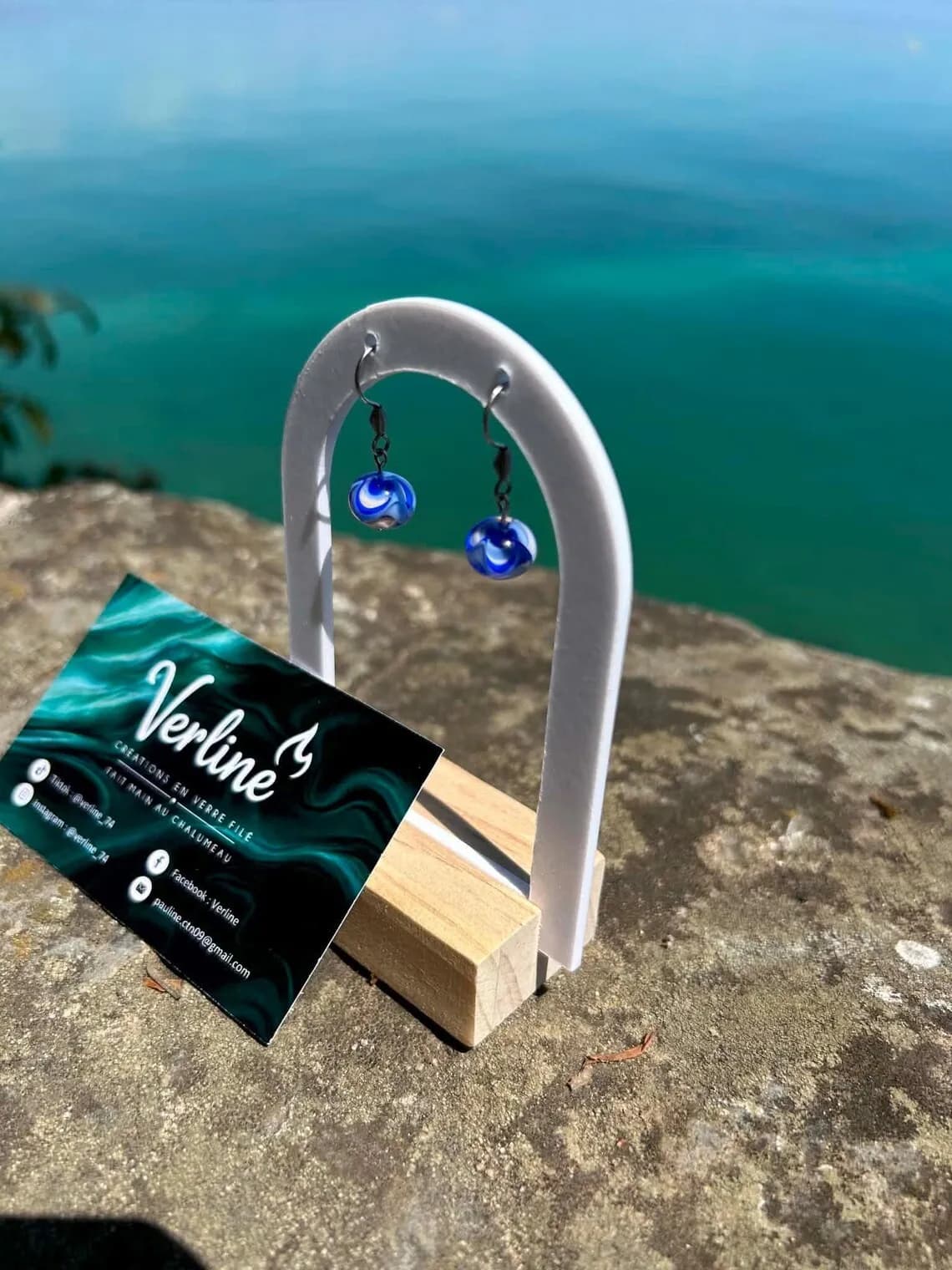 Boucles d’oreilles pendantes en verre filé bleu et blanc suspendues sur un support face à l’océan