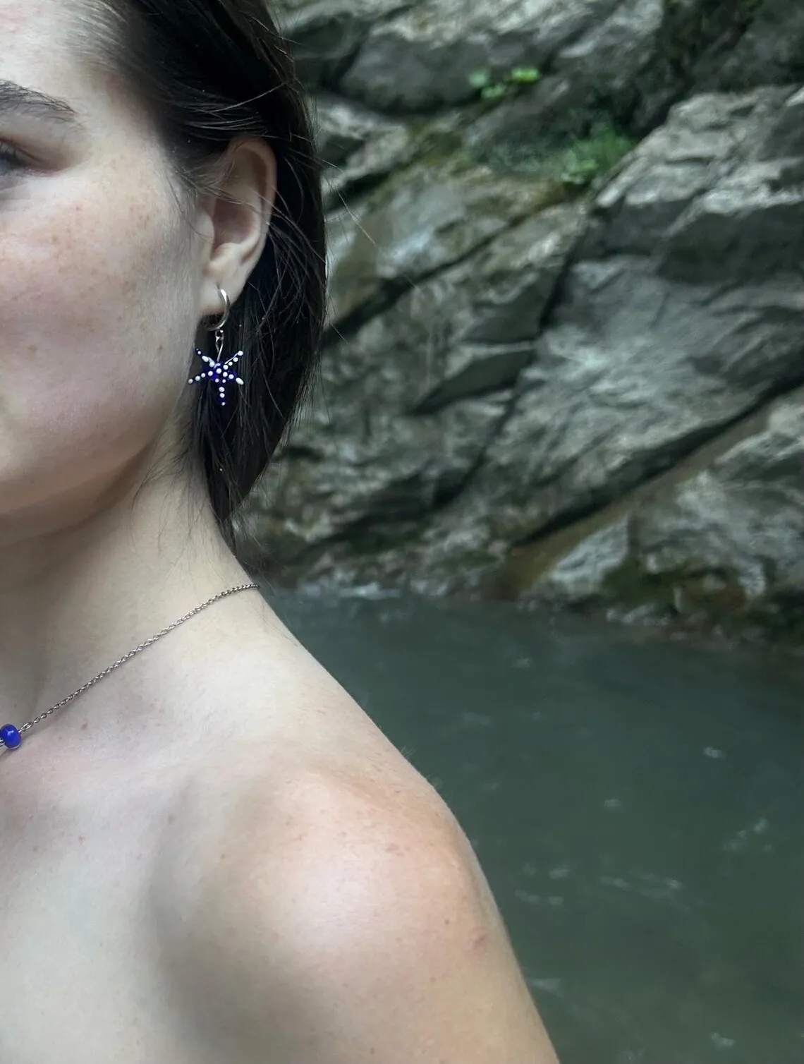 Boucle d'oreille étoile de mer bleue à pois blancs portée à l'oreille près d'un point d'eau