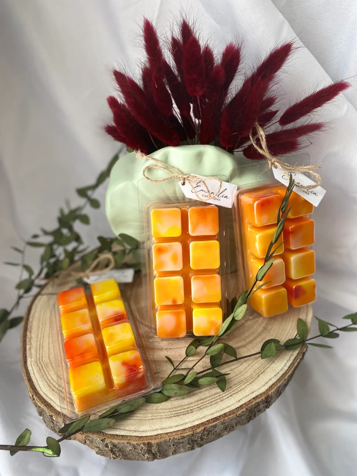 Clamshells de cire parfumée aux teintes jaune et orange marbrées, présentés sur un rondin de bois décoré.
