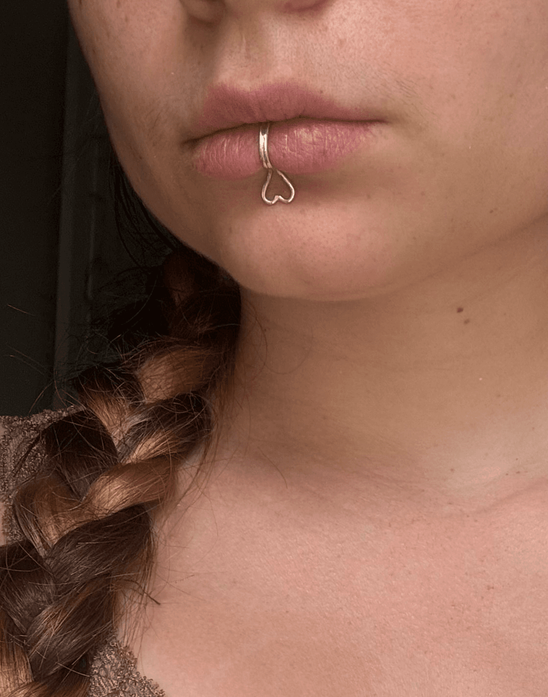 Bijou de lèvre en argent avec motif cœur pendant porté sur la lèvre inférieure, vue de trois-quarts.