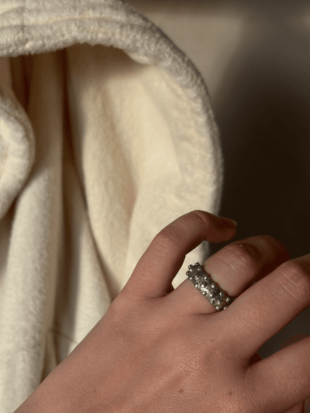 Bague argentée texturée à billes en relief portée au doigt devant de la végétation verte